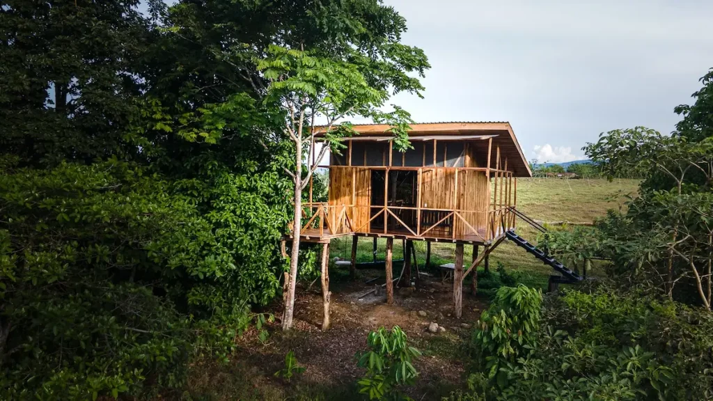 A wooden treehouse with stairs surrounded by lush greenery under a cloudy sky, perfect for where to stay in Costa Rica.